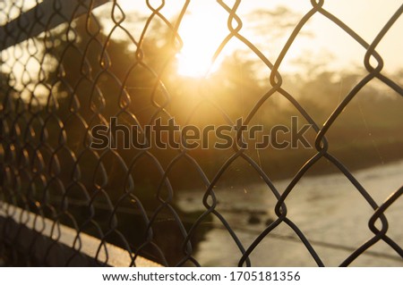 steel wire fence a suspension bridge at sunrise against the background of the river and trees. close up and blurry