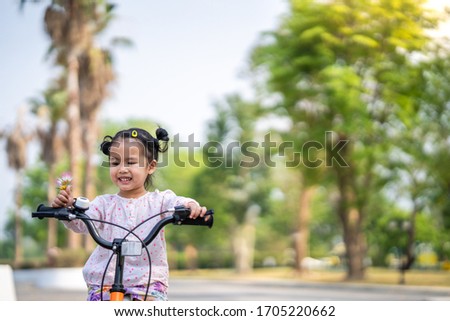 Cute asian girl wearing long sleeved pink shirt cycling on her bike at village.

