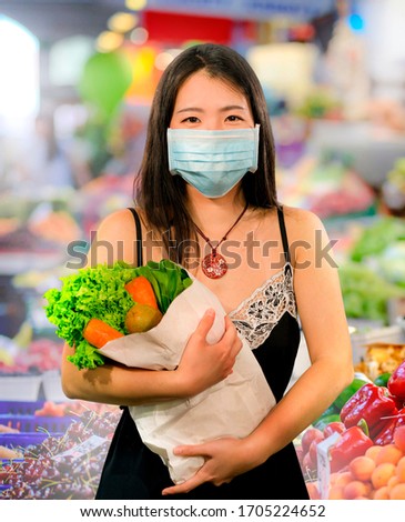 food and groceries shooping during covid-19 virus quarantine - young beautiful and positive Asian Chinese woman in face mask carrying vegetables bag stock up during coronavirus lockdown
