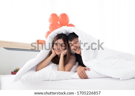 A happy young couples are in bed under the blanket after wake up in valentine's day morning in their bedroom. Young Asian couples are enjoying spending time together to celebrate Valentine's Day. Royalty-Free Stock Photo #1705226857