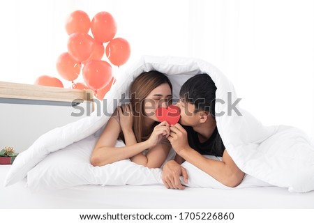 Happy young couples hold and kiss a red heart together on a bed under a blanket on morning in the bedroom. Young Asian couples are enjoying spending time together to celebrate Valentine's Day. Royalty-Free Stock Photo #1705226860