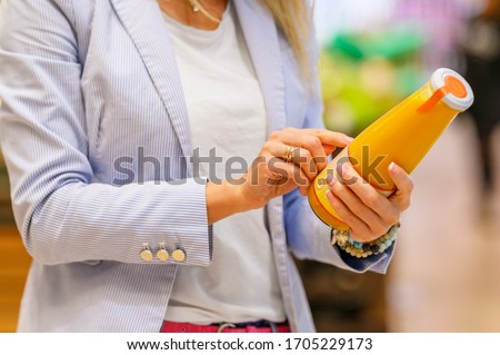 Woman reading ingredients and nutrition information on juice bottle's etiquette  Royalty-Free Stock Photo #1705229173