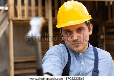Handsome builder with yellow hard hat holding a steel hammer in hand on wooden background