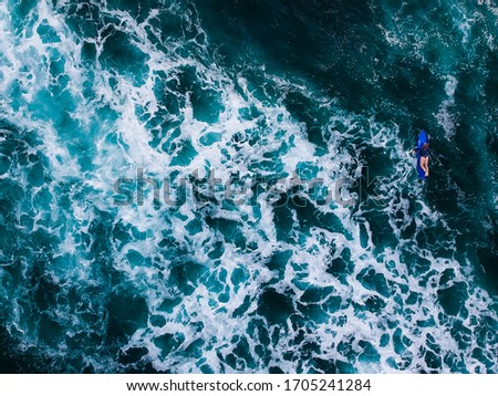 The surfer woman moving around on surfboard in the tropical blue ocean on the popular surf spot trying to catch a wave. Top view aerial drone landscape, Bali, Indonesia.