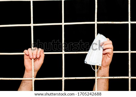 concept of restriction during a pandemic and quarantine of a person s hand behind an iron bars in his hand medical hygiene mask Royalty-Free Stock Photo #1705242688
