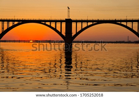 A bridge on a river lit by the sun at sunset. Evening river landscape.