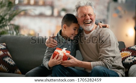 Grandpa giving his grandson birthday gift. Grandfather becomes present from grandchild. Royalty-Free Stock Photo #1705282459