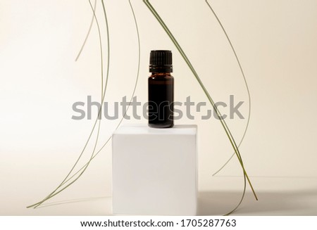 A glass bottle stands on a cube with lemongrass aromatic oil. Lemongrass leaves fall on the scent of oil. Essential oils for aromatherapy. Layout photo for your product. Pastel background