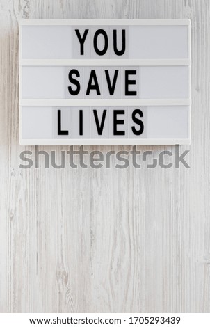 'You save lives' words on a lightbox on a white wooden surface, top view. Overhead, from above, flat lay. Copy space.