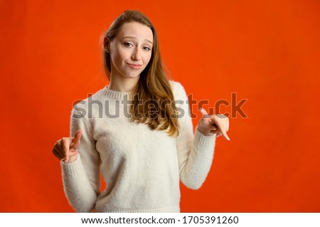 Model talking showing happy emotions showing fingers. Studio photo of a cute caucasian girl in a white sweater standing in front of the camera on a red background.