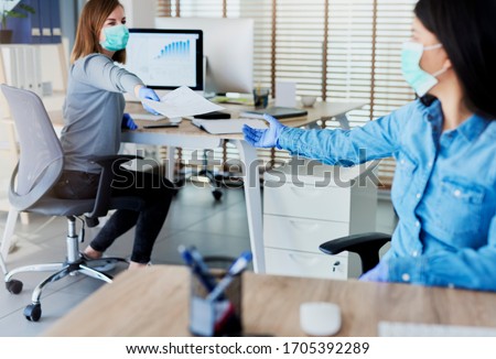 Two people in office passing documents with keeping a distance Royalty-Free Stock Photo #1705392289