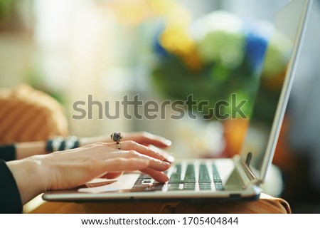 Closeup on housewife in the house in sunny day surfing web on a laptop. typing on keyboard