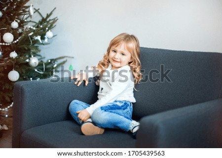 Interesting little girl sits on chair. Merry Christmas and Happy New Year. Lovely baby enjoy christmas. Childhood memories. Little child celebrate christmas at home. Family holiday.