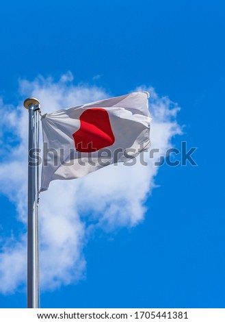 Japanese National Flag waving in the wind against a sunny blue sky.