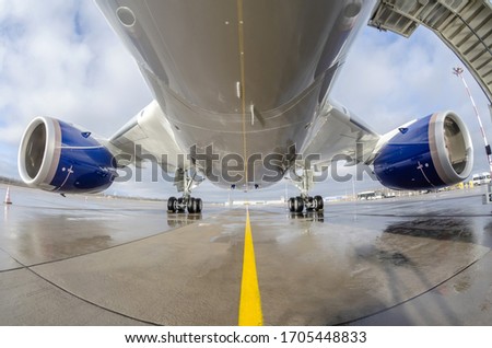 Passenger wide-body plane is parked on the airport apron. Aircraft fuselage, engine and main landing gear Royalty-Free Stock Photo #1705448833