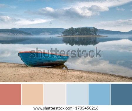 Beautiful landscape, bright blue fisherman boat on orange beige sand, grey clouds in light blue sky over lake. Color palette swatches, pastel fashion trends in color combination inspired by nature.