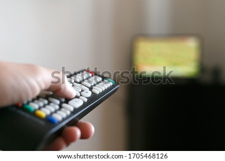 A man holds in his hand the remote control from the TV and switches channels. Against the background of a television with a blurry image.