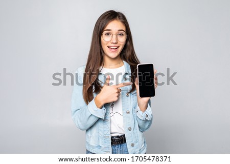 Happy beautiful young woman with long curly hair holding blank screen mobile phone and pointing finger over white background Royalty-Free Stock Photo #1705478371