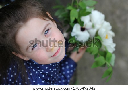 beautiful young girl with long brown hair and a blue jacket with a white bouquet of peonies is standing in the yard
