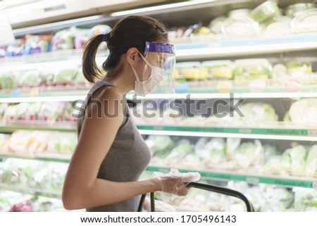 Woman wearing gloves, face shield and mask choosing vegetables. Panic shopping during the corona virus pandemic.