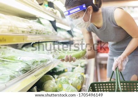 Woman wearing gloves, face shield and mask choosing vegetables. Panic shopping during the corona virus pandemic.
