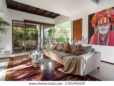 Concept of stylish interior at lounge room. Cozy house with ethnic decor, comfortable sofa, cushions, woven ornamental carpet, plants and painting on wall Royalty-Free Stock Photo #1705496509