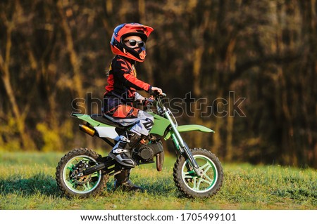 Child on his small motorcycle. Small biker dressed in a protective suit and helmet. The kid is engaged in motocross.