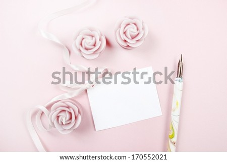 Paper card decorated with pink bow, vintage pen and roses on wooden background. Top view, copy space