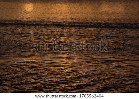 Mysterious waves of water in golden sunbeams on sunset, abstract background.