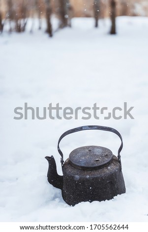 Black camp kettle in the snow. Black teapot on a white background. A blackened teapot on a winter picnic