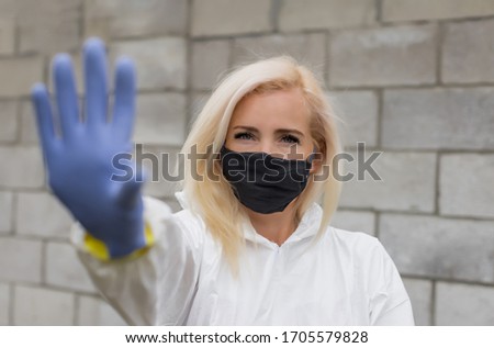 Woman in mask, white protective suit and gloves making sigh stop
