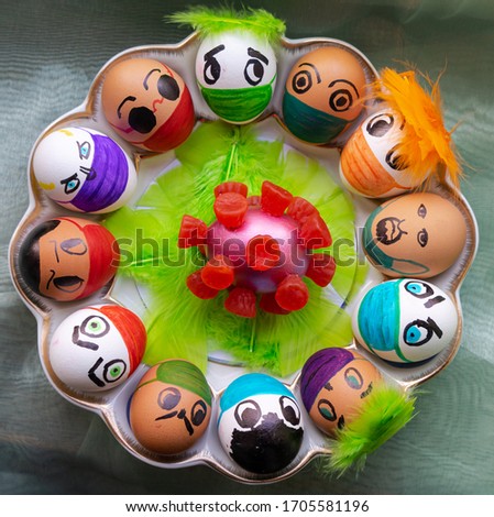 Plate with 12 Easter eggs arranged in a circle and decorated with painted protective masks from the coronavirus and colorful feathers. In the center is an egg decorated with sweets like a coronavirus.