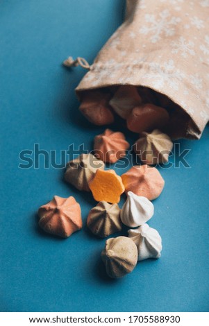 Colorful meringues and a small cloth bag decorated with white snowflakes on a blue background. Selective focus.