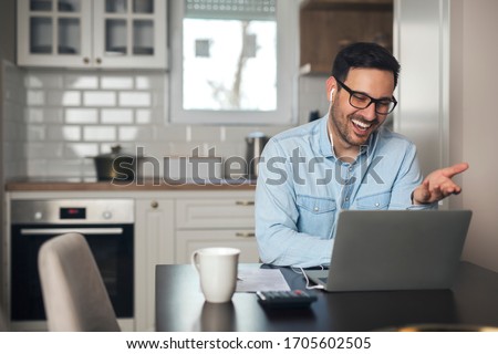 A young man working remotely heaving a meeting on a laptop while wearing headphones. Royalty-Free Stock Photo #1705602505