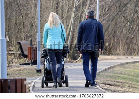 Couple with a baby stroller walking in spring park near the residential buildings. Quarantine in a city during covid-19 coronavirus pandemic, concept of motherhood, parents with pram