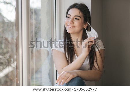 Young woman take off protective mask. Female in white t-shirt and white medical mask. End of quarantine. Coronavirus theme Royalty-Free Stock Photo #1705652977