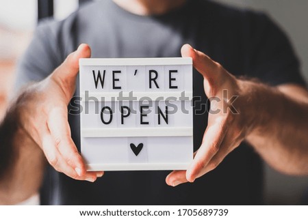 End of quarantine. Man holding lightbox with greeting text message We're open in his hands. Hotel, cafe, local shop, service owner welcoming guests after coronavirus outbreak and people shutdown. Royalty-Free Stock Photo #1705689739