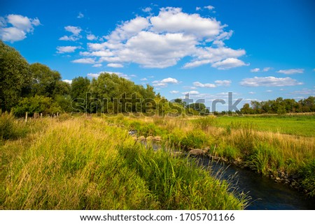 Panoramic image of a green meadow and blue Sky, with a river in the foreground