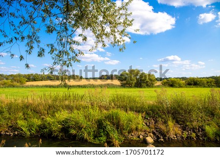 Panoramic image of a green meadow and blue Sky, with a river in the foreground