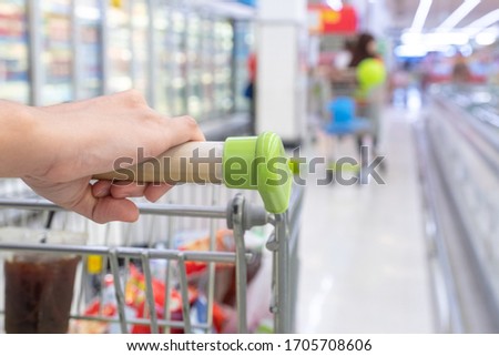 Selective focus woman hand holding shopping cart in super market or  convenience store concept and shelves in frozen food corner on blurry for background