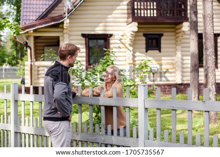 Middle aged man meeting smiling female neighbor in countryside and talking cheerfully to her over fence Royalty-Free Stock Photo #1705735567