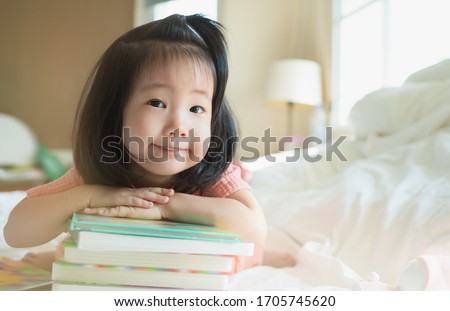 Image of Asian Toddler portrait shot while her proud and talking to present her book stack, Concept little bookworms enjoy learning to be intelligent kid, Adorable child reading book for homeschooling