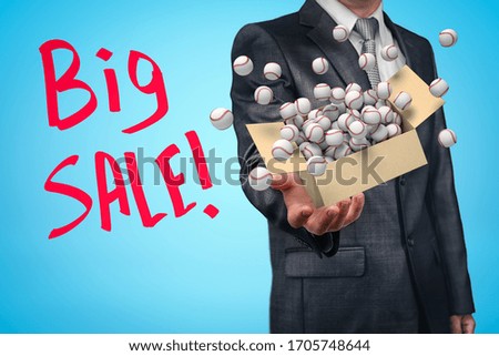 Anonymous businessman levitating cardboard box full of baseballs that are flying out of it on blue background with title 'Big SALE'. Sports equipment. Seasonal sales.