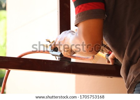 Close​ up​ hands​ of​ welder is welding the various parts of the house construction.Erecting technical steel for background.
