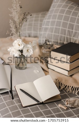 Cosy picture of notebook with pen, wooden pile, flowers and books on a bed