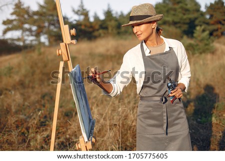 Woman in a summer field. Lady drawing. Woman in a apron and hat.
