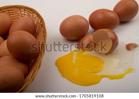 Chicken eggs in a wicker basket, a broken chicken egg and scattered eggs on a white background. Close up.