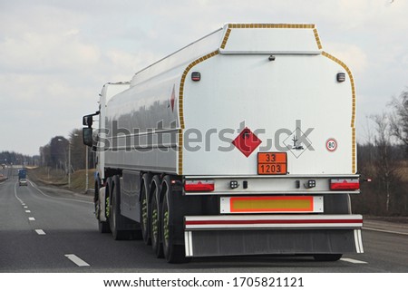 White semi truck fuel tanker with 33/1203 dangerous class sign and copy space place blank on barrel drive on asphalt highway on a spring day on blue sky background, side rear view ADR hazardous cargo