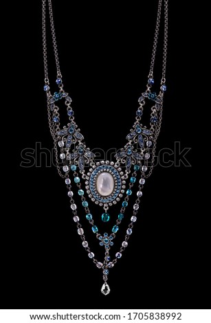 Photo of an aged artistic vintage old fashioned in Indian style necklace jewellery with abstract flowers and small balls with blue diamonds and white pearl stones with metal parts on black background 
