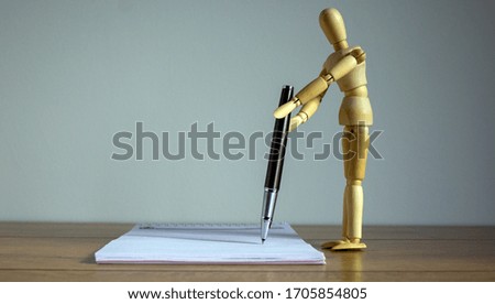 Notebook and wooden man model with pen on wood table.